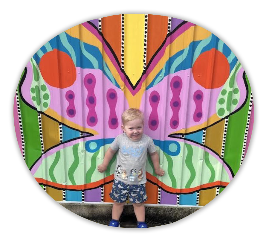 A smiling child standing in front of a butterfly wings mural.