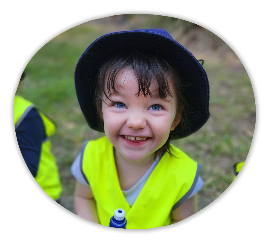 A child sitting in nature in a hi-vis vest smiling.