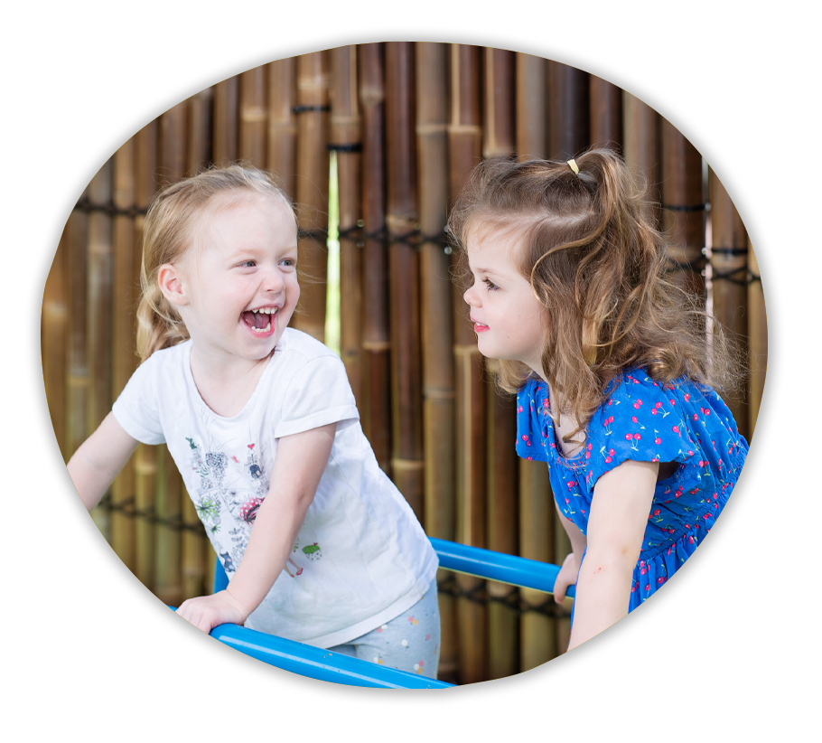 Two children smiling with glee on a small bridge in a playground