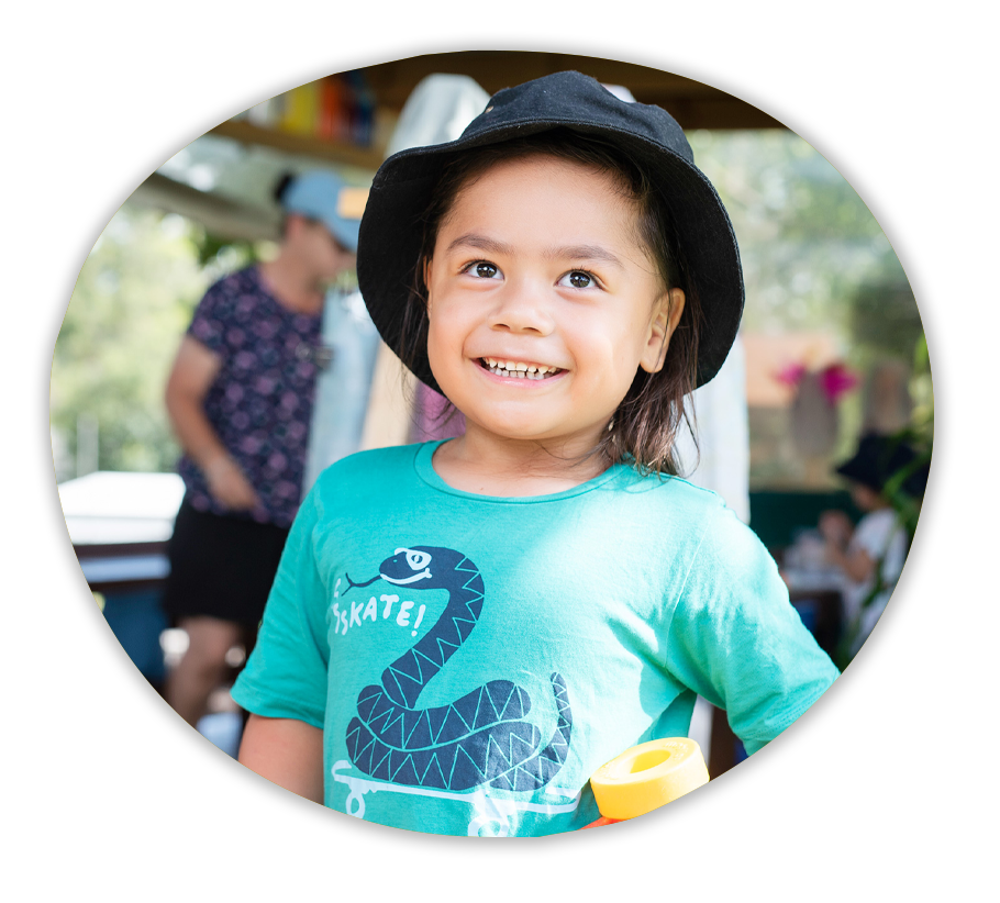 A child in a teal shirt standing in a playground, smiling.