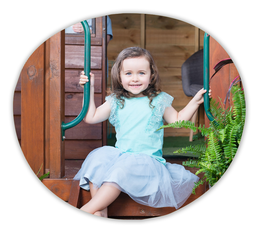 A child sitting on the steps of a cubby house smiling happily.