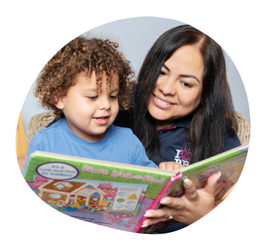 Two children sitting on a chair smiling as they read a book together.
