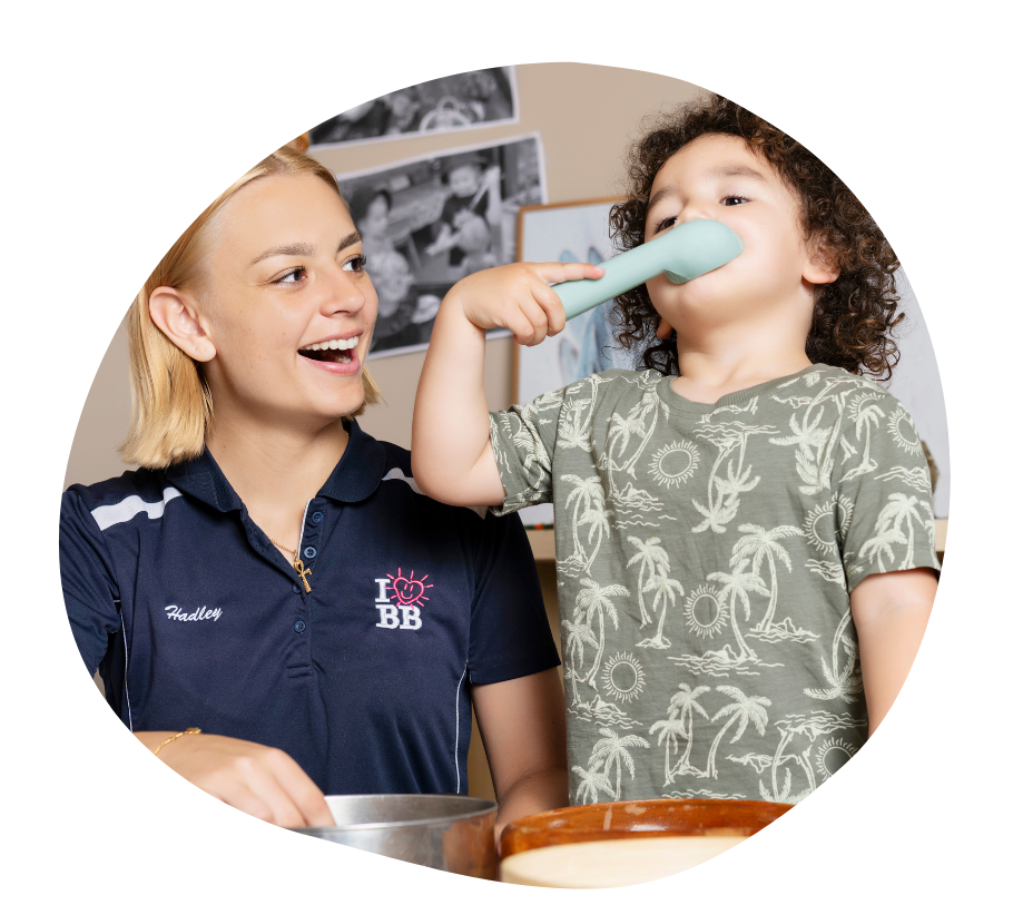 Two children sitting on a chair smiling as they read a book together.